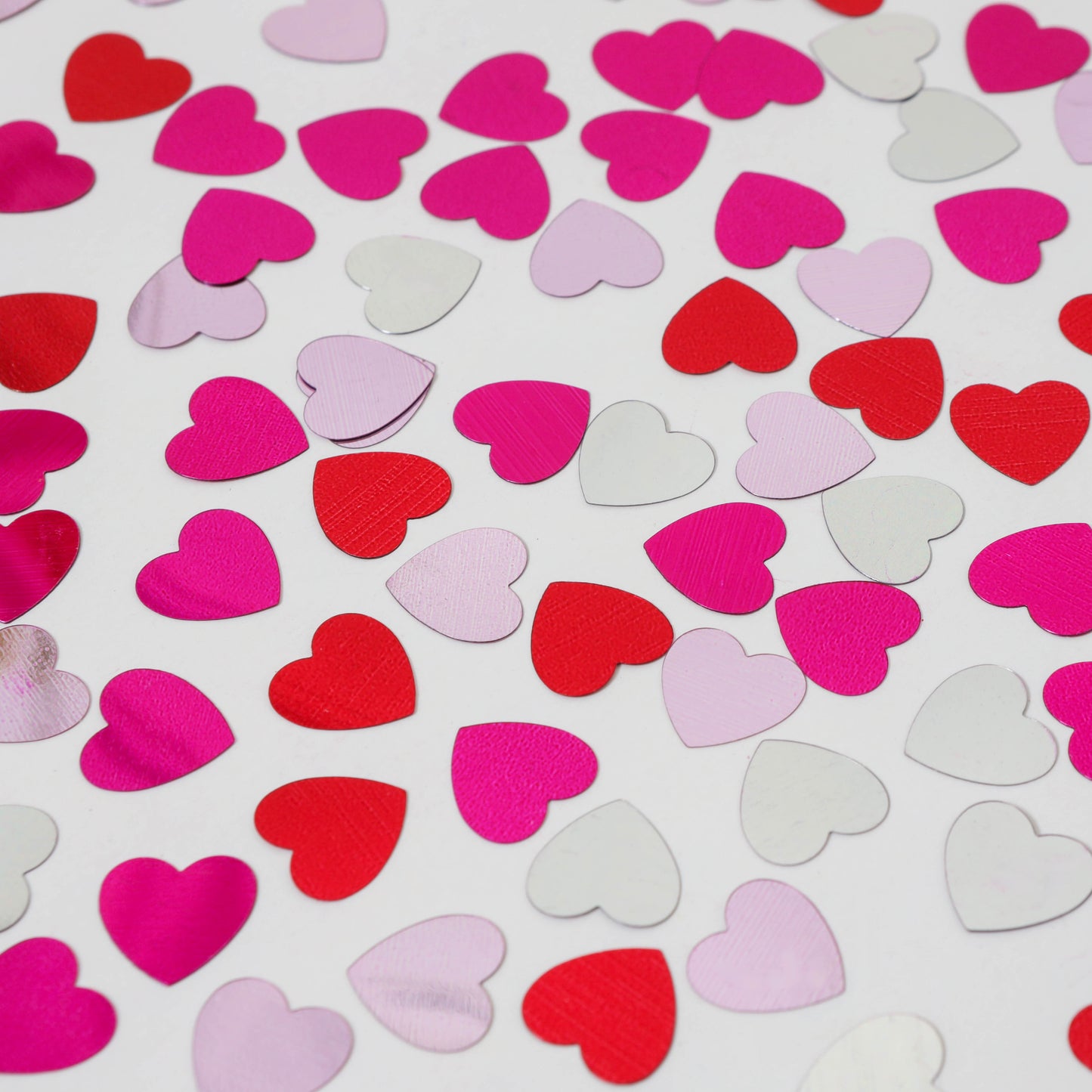 Multi-color heart shaped confetti scattered on white background showing pink red and white hearts