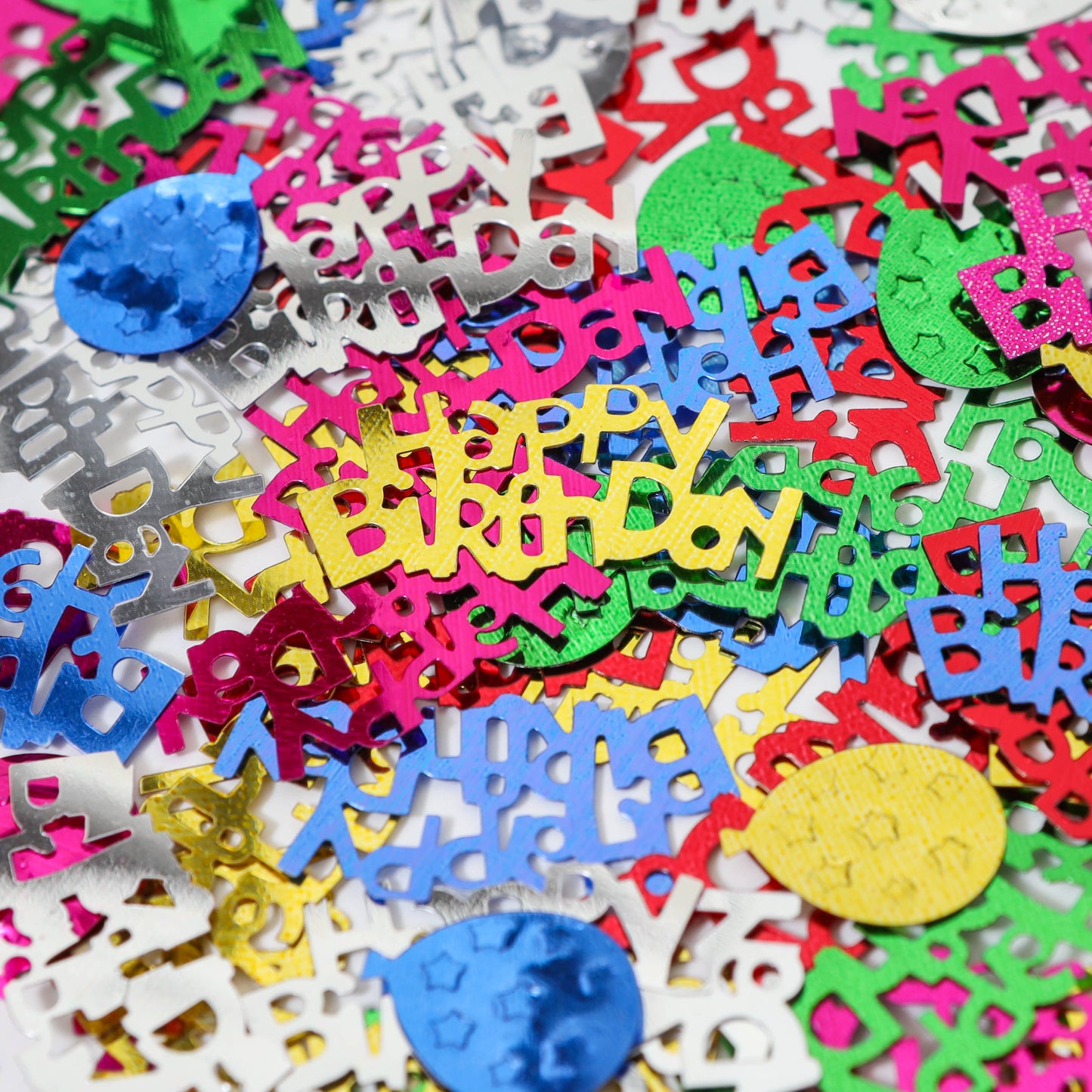 Close-up view of layered metallic Happy Birthday confetti and balloon shapes in mixed colors piled together.