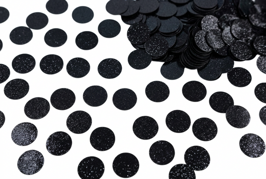 Luxe black circle confetti scattered on a white background with additional stacked pieces in the corner