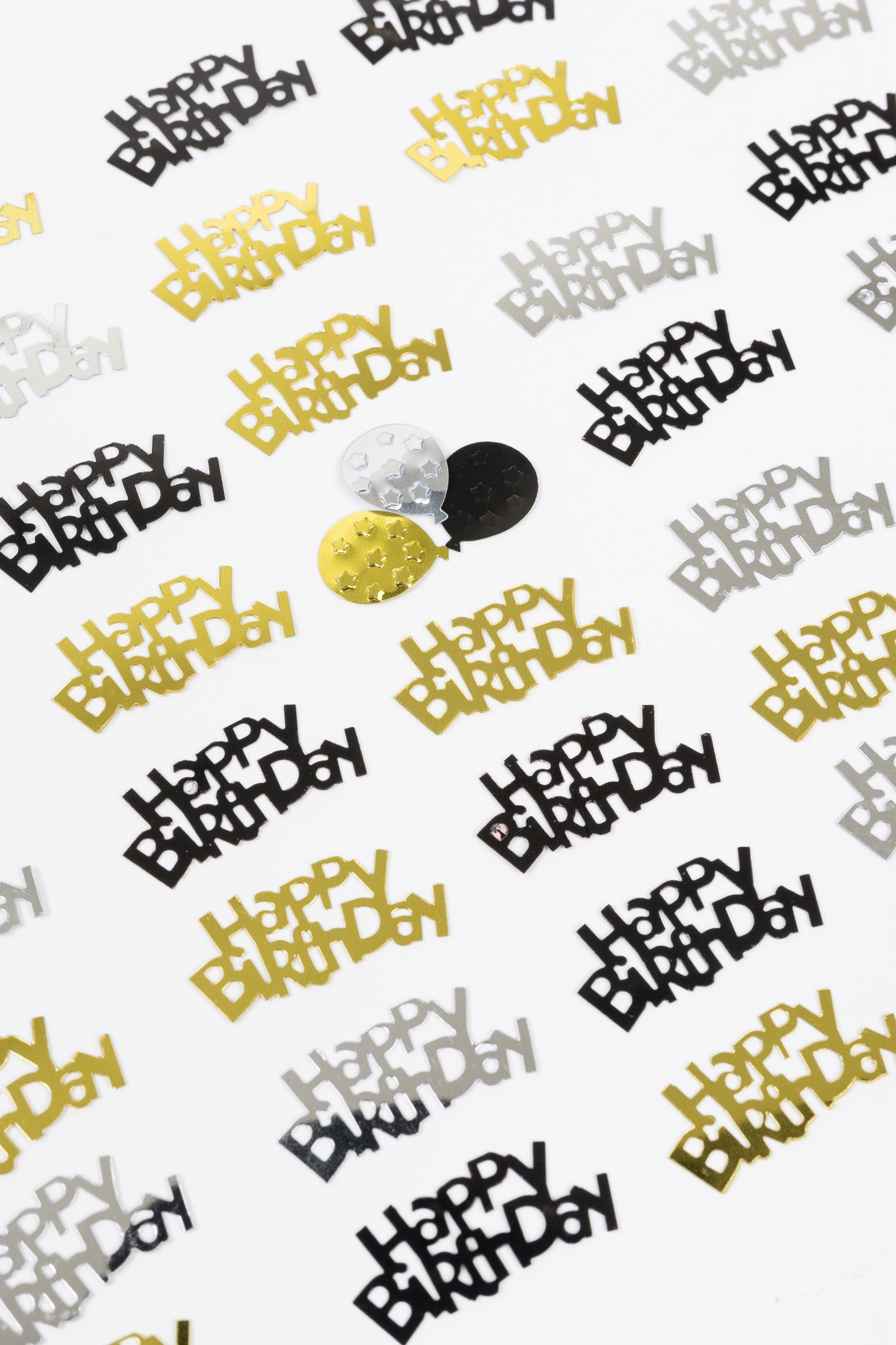 Metallic Happy Birthday confetti in black, gold, and silver arranged in a flat lay on a white background