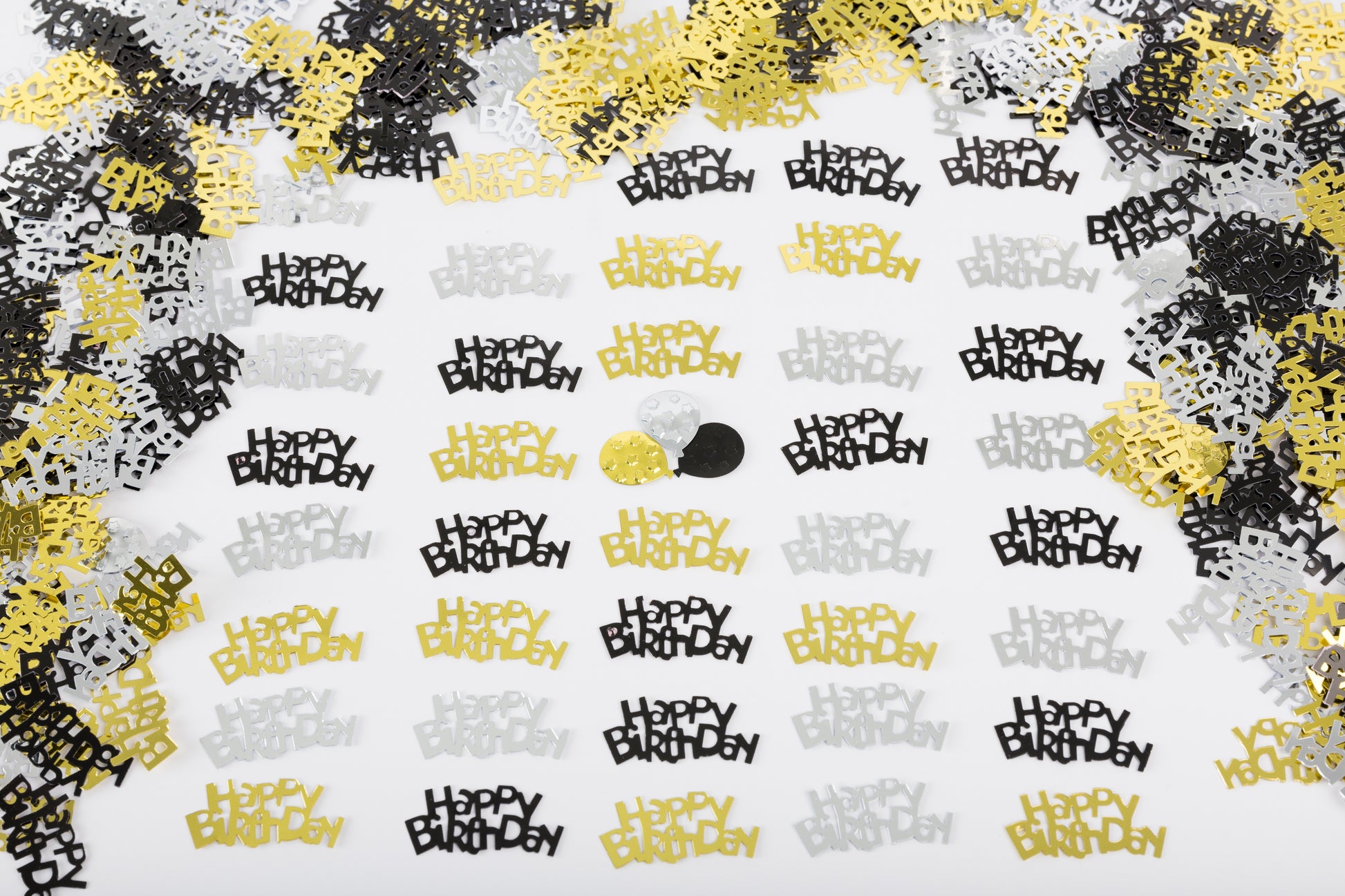Metallic Happy Birthday confetti in black, gold, and silver evenly scattered on a white background